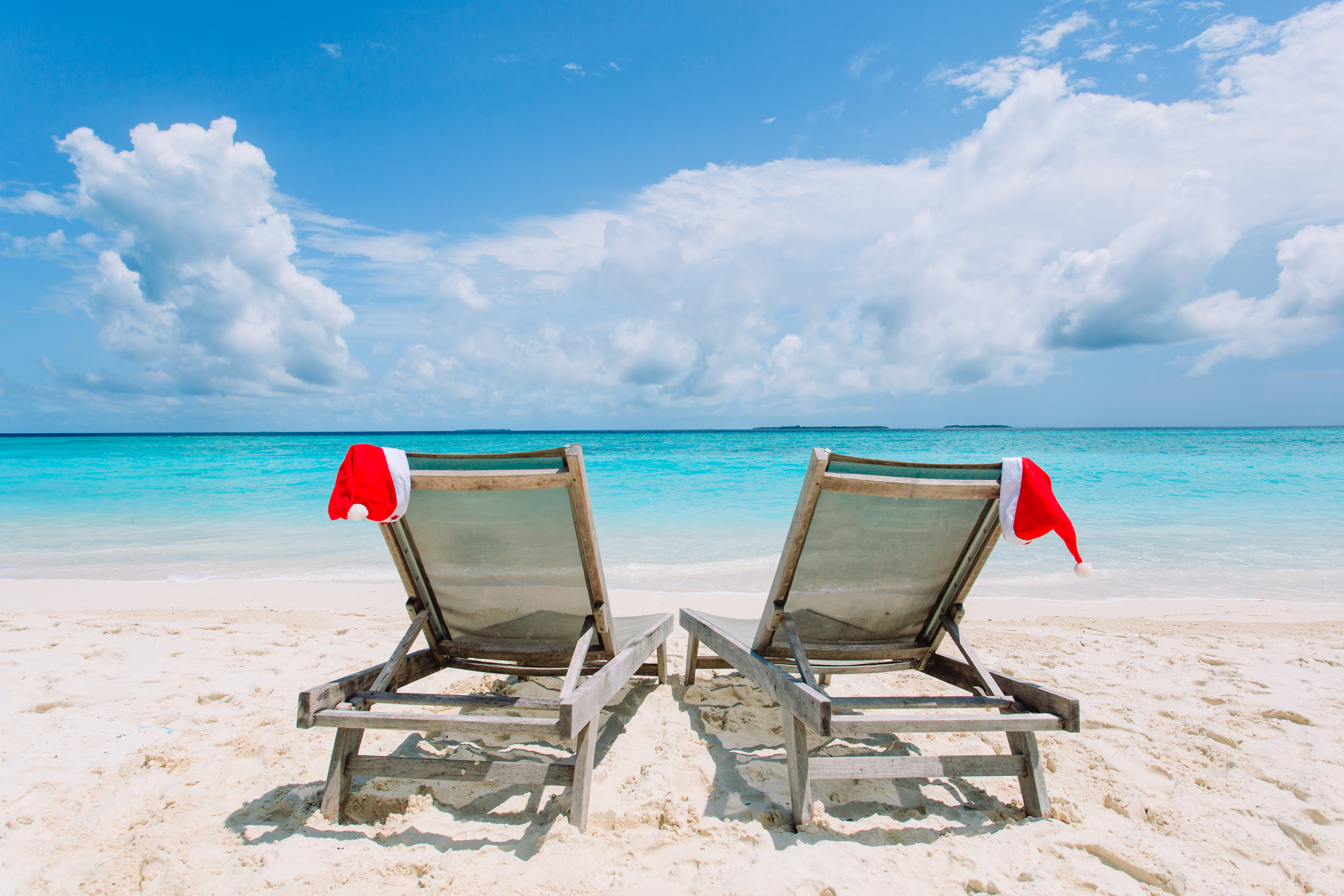 two sun loungers with christmas hats on a beach
